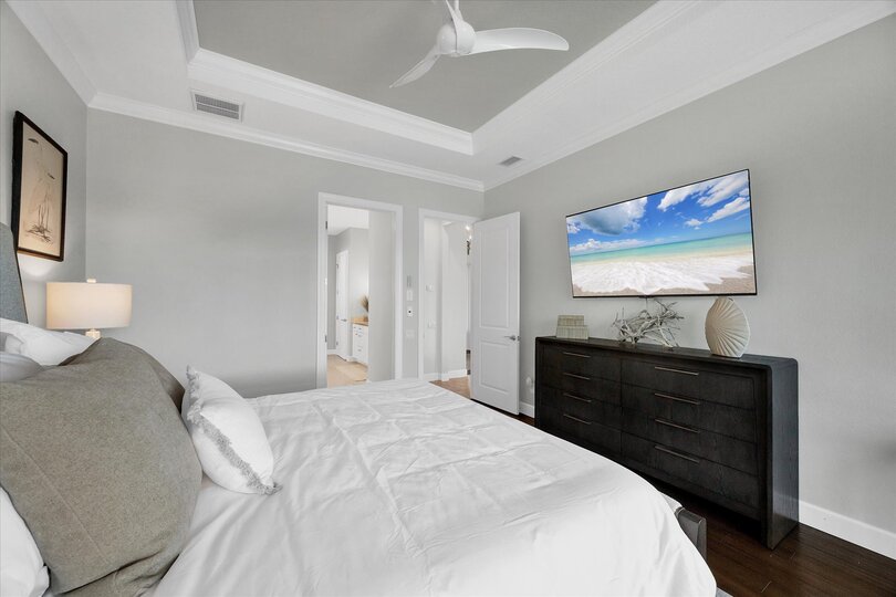 Primary bedroom features king bed, attached bathroom, desk & chair, 65-inch Smart TV, and beautiful view of pool and canal